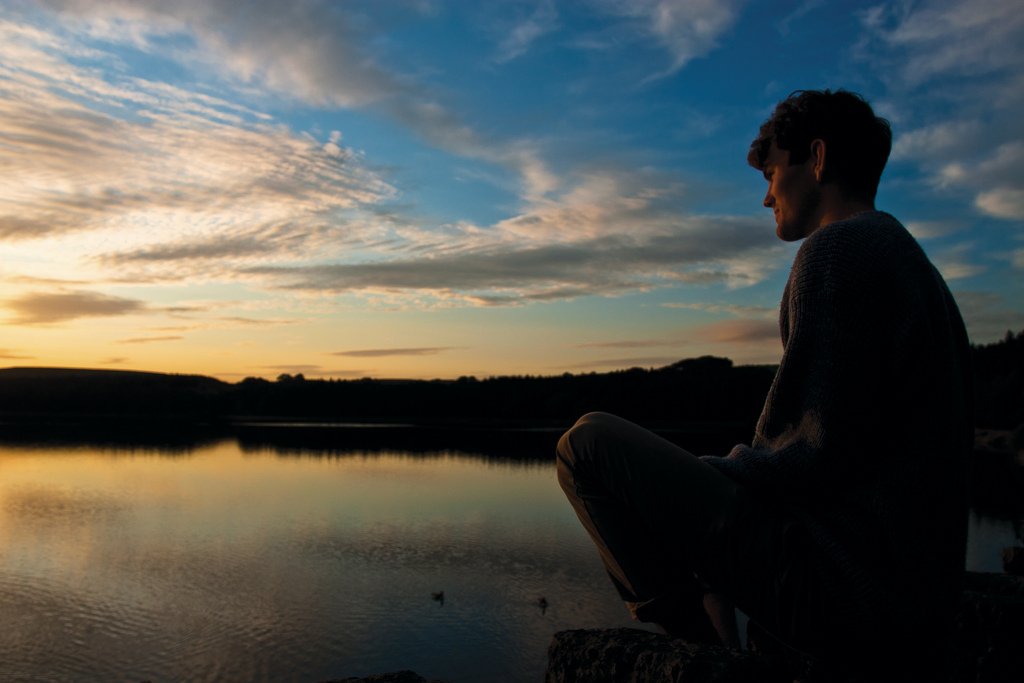 man lake water sky clouds thinking pensive reflection sunset