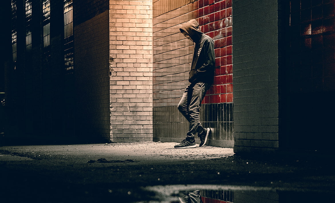 Young man leans against a lit wall at night.