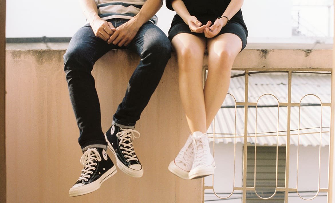 A young man and woman sitting on a railing. Their hands look like they're having a deep conversation.