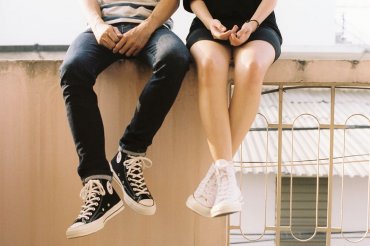 A young man and woman sitting on a railing. Their hands look like they're having a deep conversation.