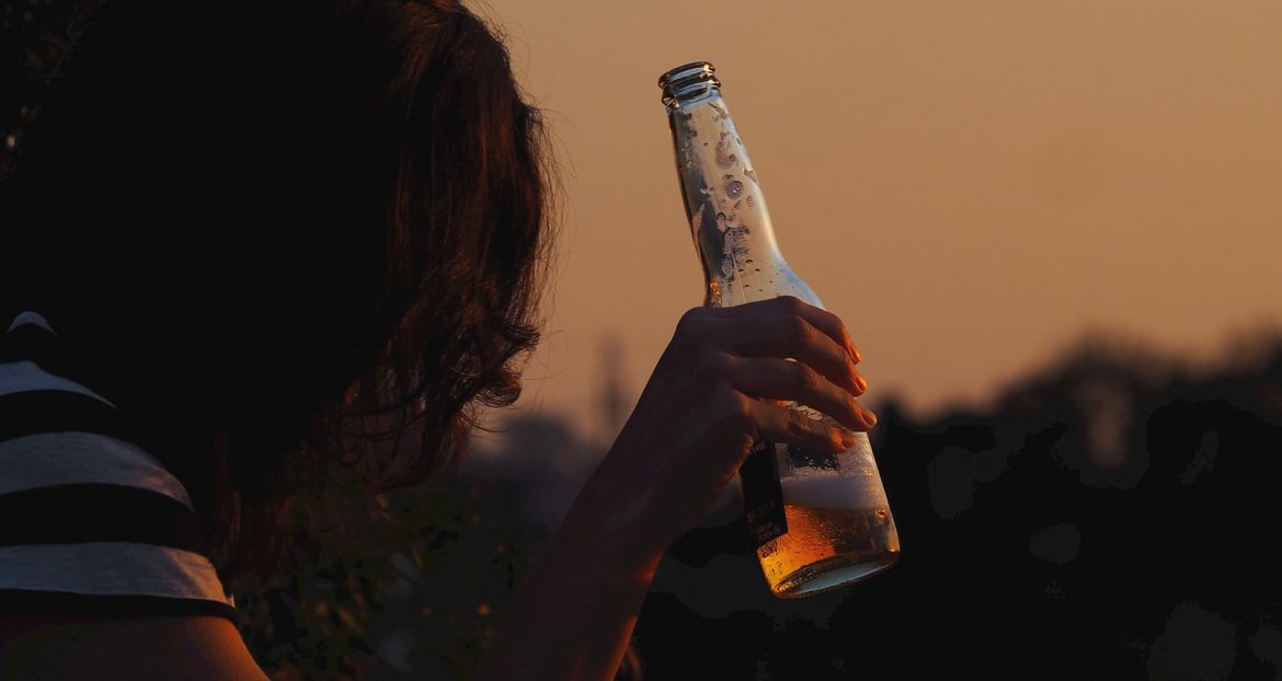 Young woman holding a beer bottle at sunset.