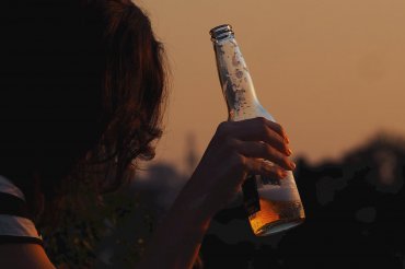 Young woman holding a beer bottle at sunset.