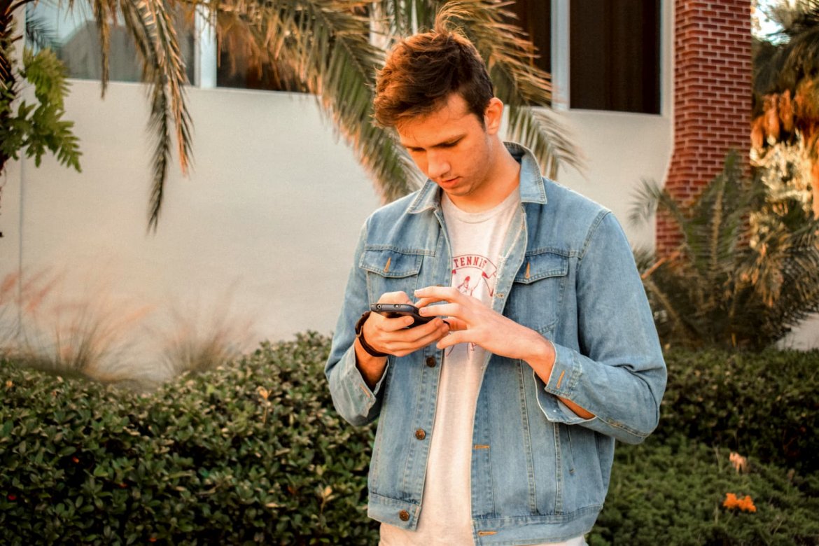 a young man wearing a denim jacket reading something on his phone.