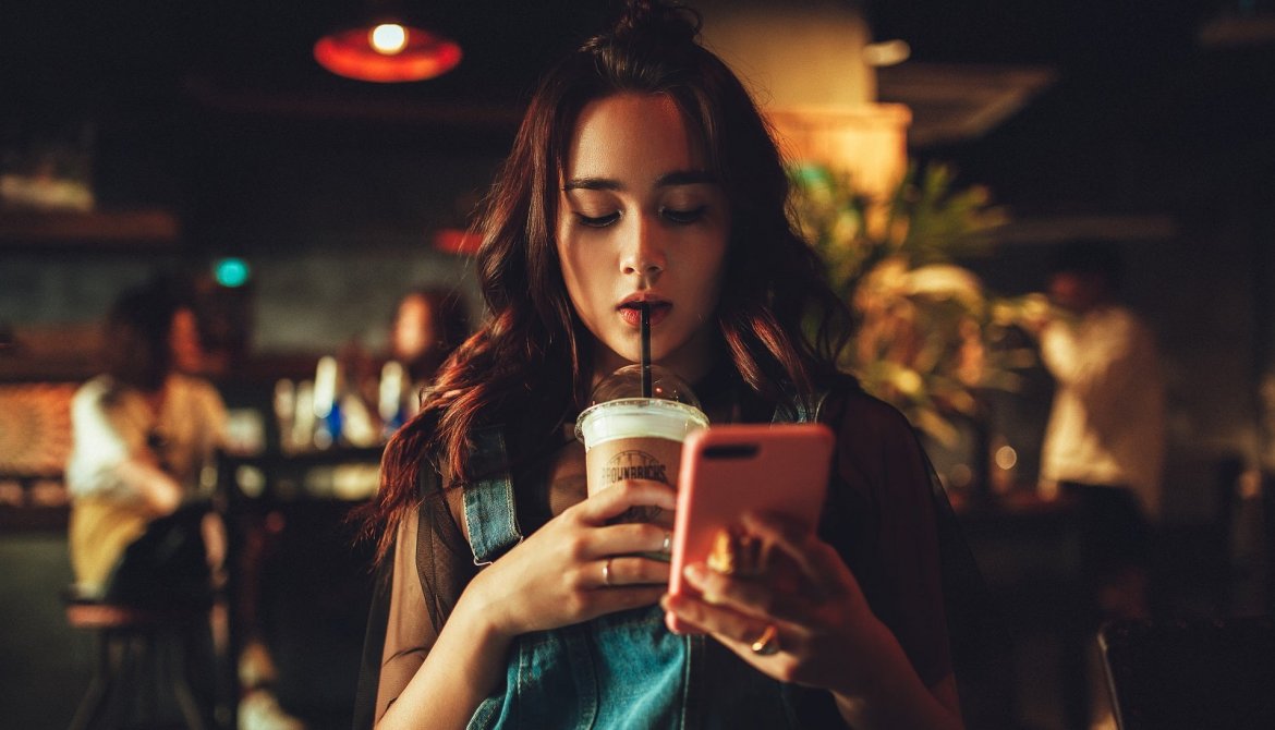 A teen girl is engrossed by her phone as she drinks in a coffee shop.